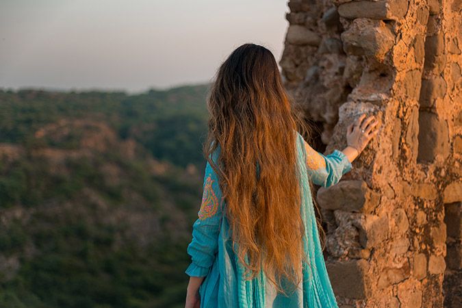 Back view of a girl in Pakistani dress viewing the green mountains 