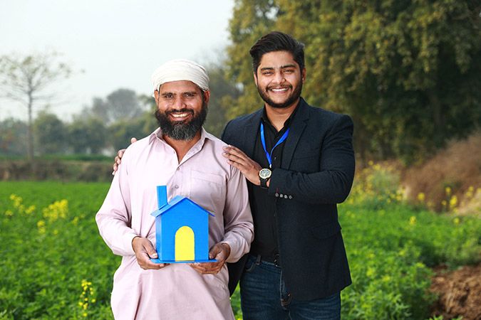 old man smiling and holding a house prop in hands while standing with a banker
