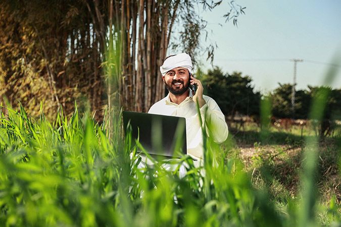 Man in traditional clothes smiling, holding a laptop while taking call on mobile phone