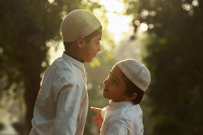 Two kids in traditional clothes wearing muslim cap