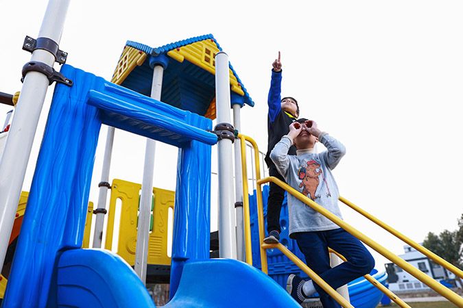 Kids standing on slide stairs, one is pointing at the sky while other is looking through hands