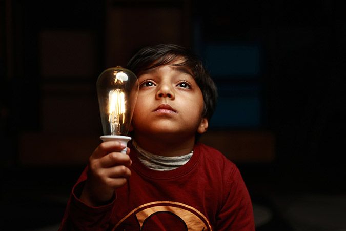 Kid looking up while holding a turned on bulb