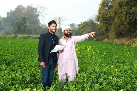 Banker holding a paper in hand while standing with a farmer who is pointing in some direction