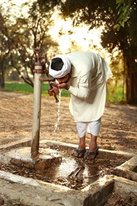 man in traditional clothes drinking water from a old water pum