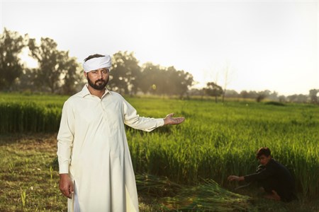Man in traditional clothes pointing at fields with a farmer working in background