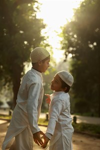 Two kids in traditional clothes wearing muslim cap