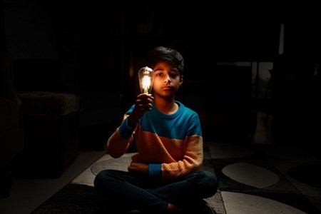 Kid holding a turned on light bulb in hand with serious face