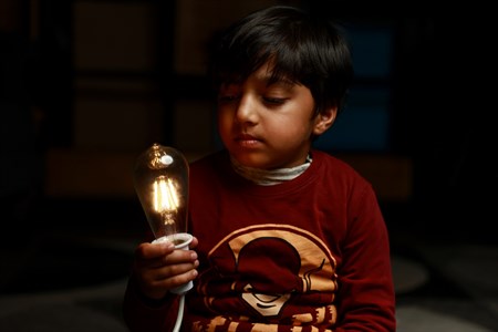 Kid looking at a turned on bulb while holding it