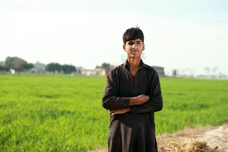 Boy standing with folded arms with fields as background