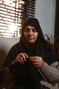 Old woman wearing hijab and knitting with black thread
