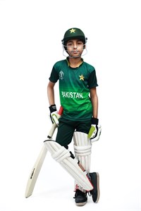Kid standing with bat in pakistani cricket kit
