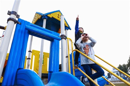 Kids standing on slide stairs, one is pointing at the sky while other is looking through hands
