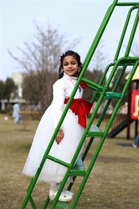 Little girl in white dress climbing slide stairs in park