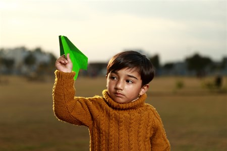 Little boy holding a green paper plane in the air