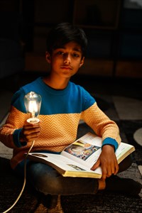 Kid holding a turned on light bulb and book