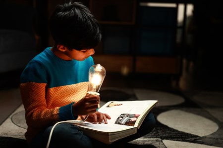 Kid faking studying while holding a turned on light bulb and book