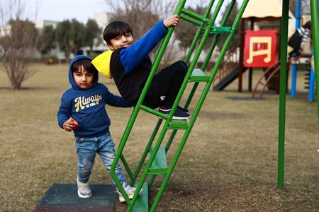 Two kids playing in park, one is climbing stairs