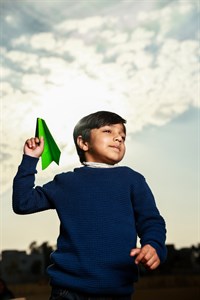 Little boy holding a green paper plane in the air