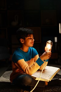 Kid looking at turned on light bulb and holding a book