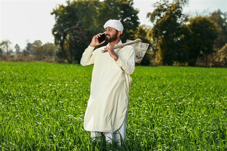 Farmer holding grape hoe on his shoulder while taking call on mobile phone