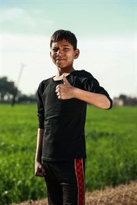 Boy giving thumbs up standing with fields as background