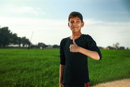 Boy giving thumbs up standing with fields as background