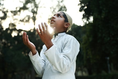 Kid praying with hands in the air wearing traditional clothes and looking up in the sky